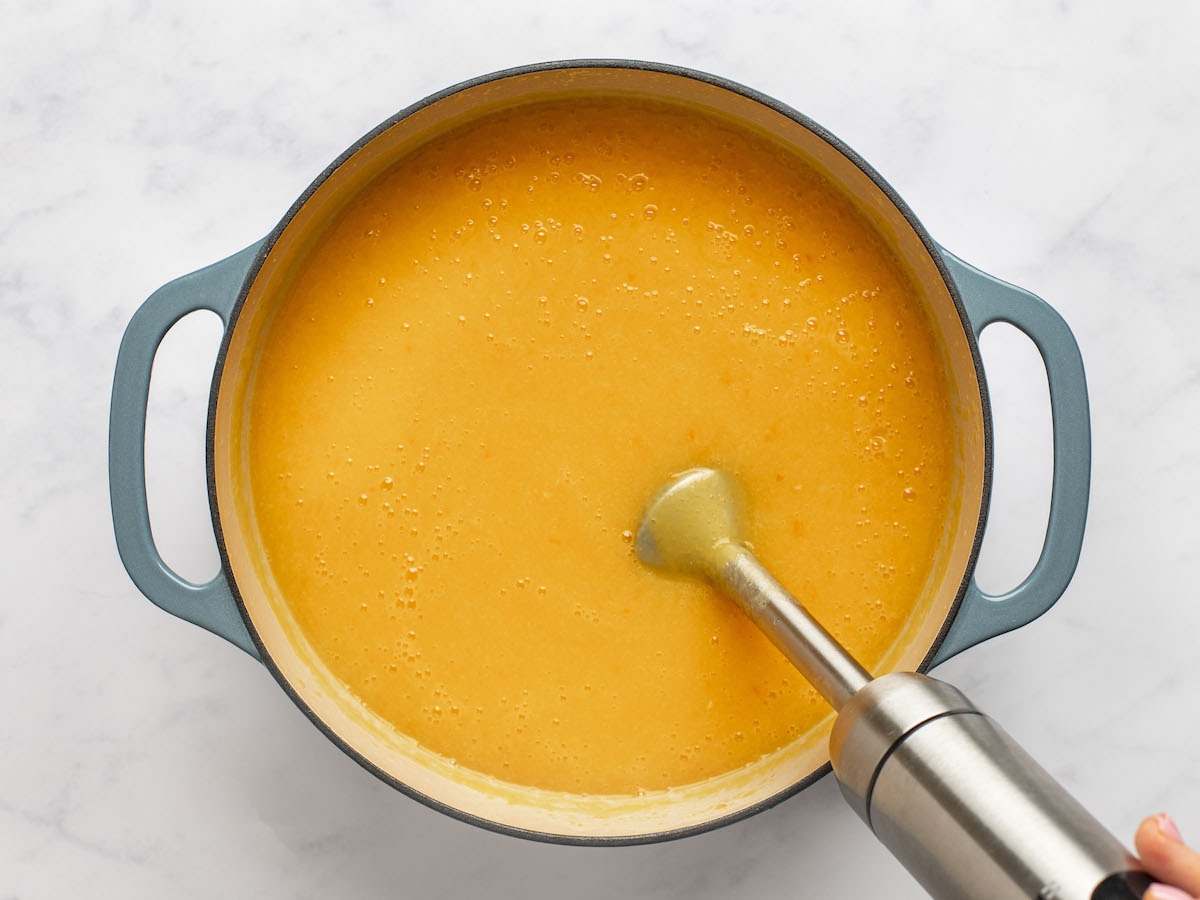 Immersion blender in a pot of orange soup.