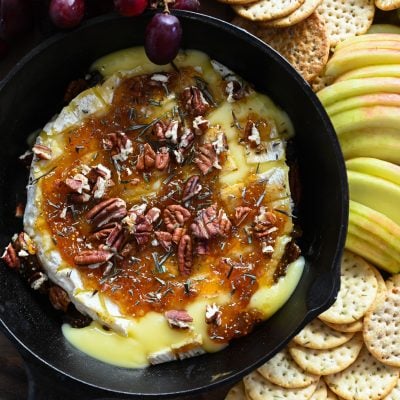 baked brie with crackers, apples, and grapes on wood board