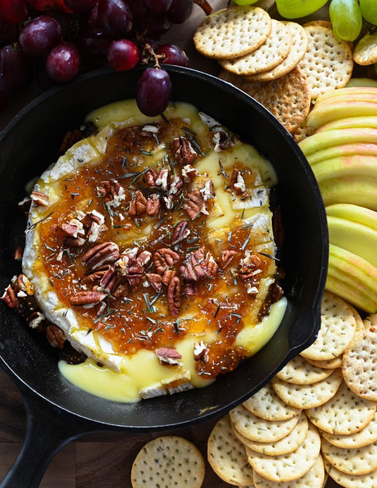 baked brie with crackers, apples, and grapes on wood board