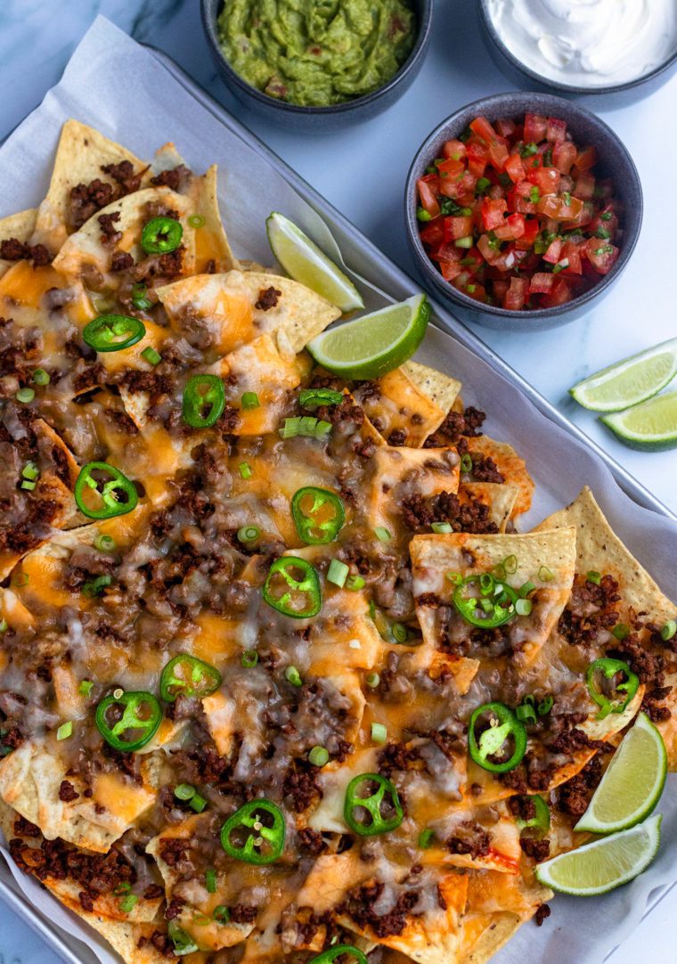 beef nachos on sheet pan with salsa, guacamole, and sour cream