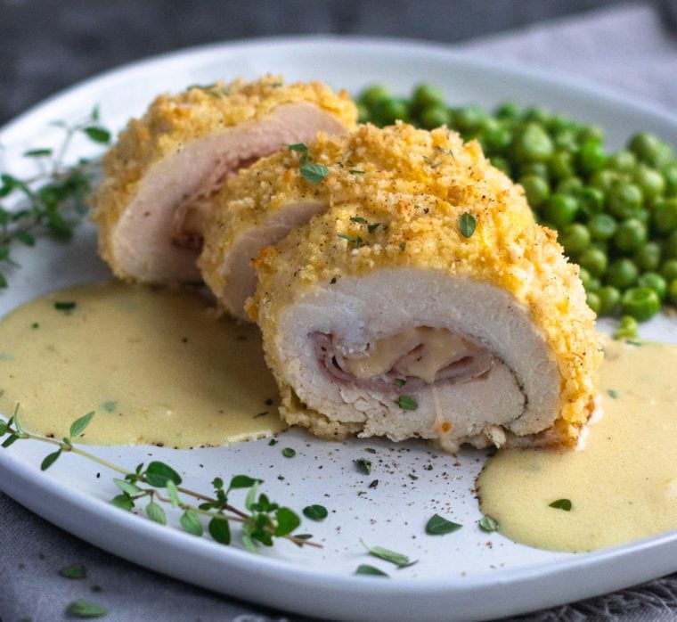 chicken cordon bleu with sauce and peas on plate