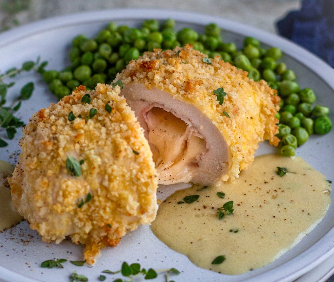 chicken cordon bleu with sauce and peas on plate
