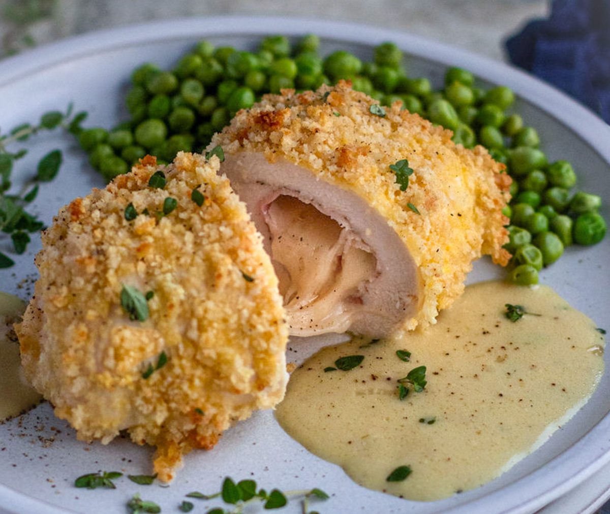 Halved chicken cordon bleu on a plate with peas.