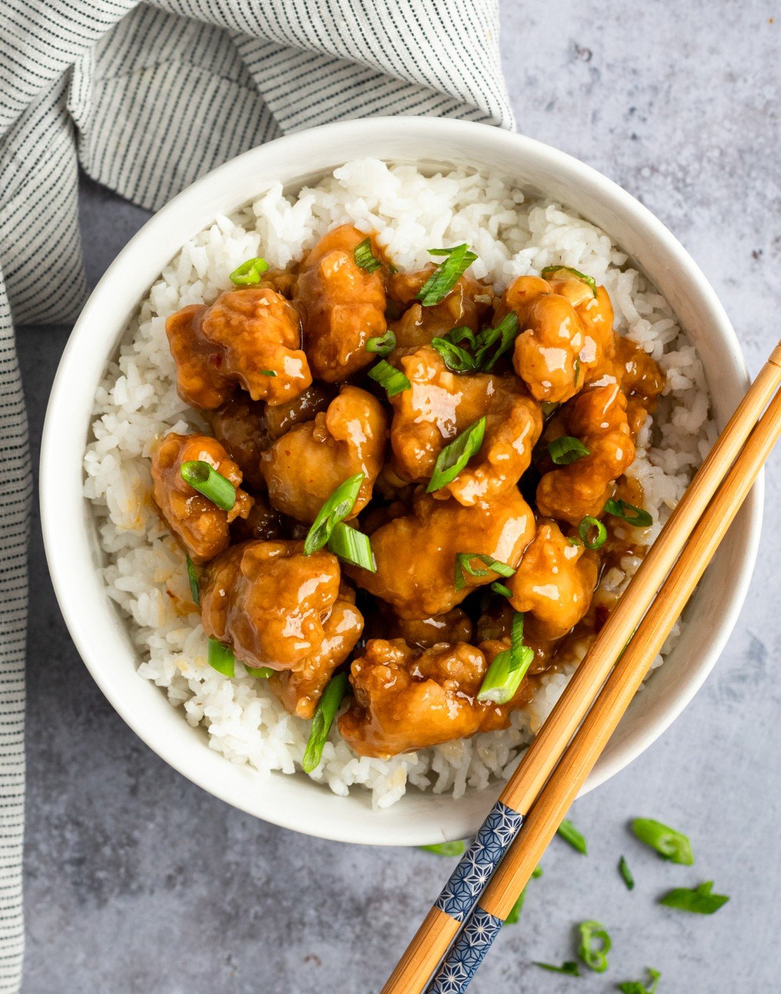 orange chicken in bowl with rice and chopsticks