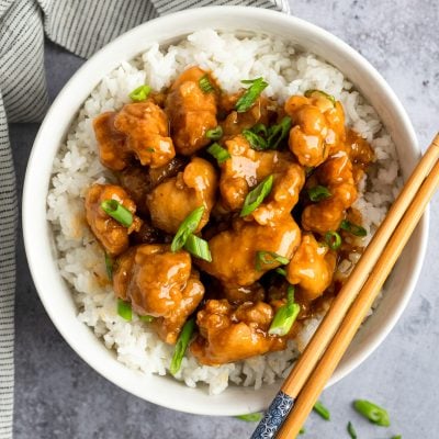 orange chicken in bowl with rice and chopsticks