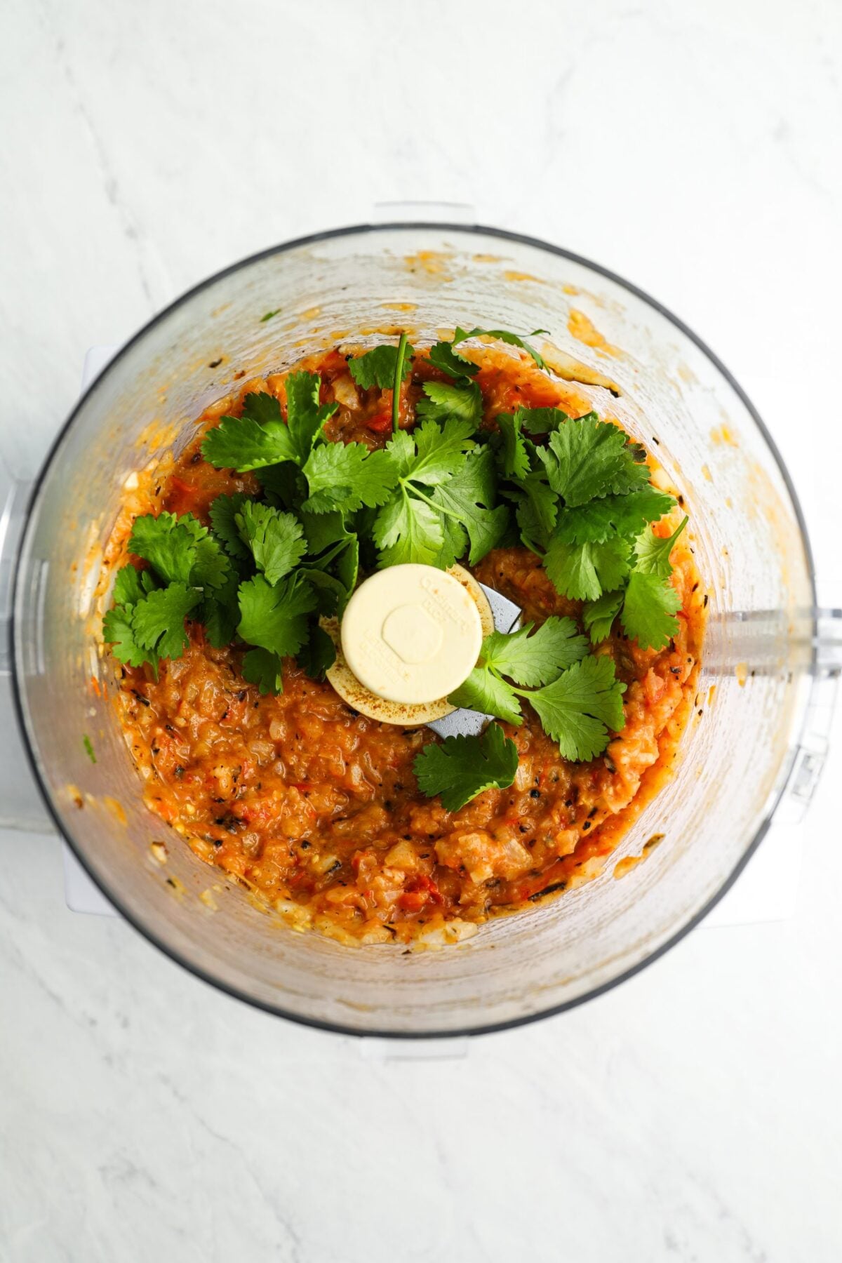 adding cilantro to blended vegetables in food processor.