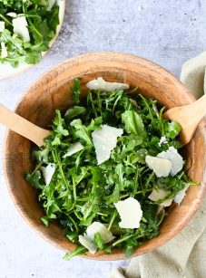 arugula salad in wooden bowl with wooden spoons.
