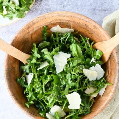arugula salad in wooden bowl with wooden spoons.