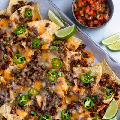 beef nachos on sheet pan with salsa, guacamole, and sour cream.