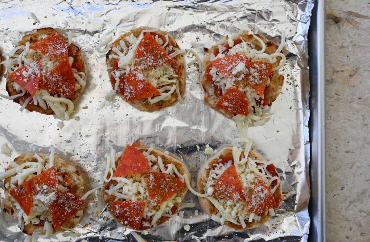 English muffins topped with cheese and pepperoni on baking sheet