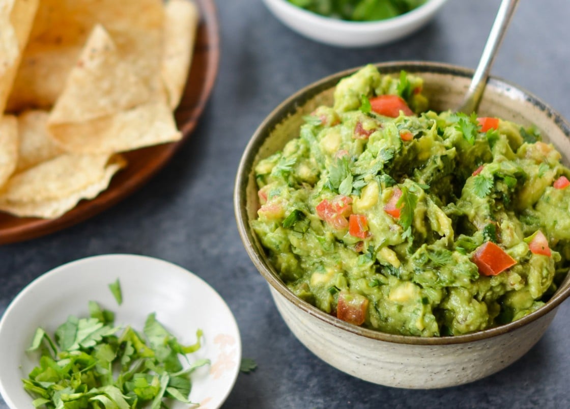 A bowl of guacamole with chips on a table.