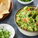 A bowl of guacamole with chips on a table.