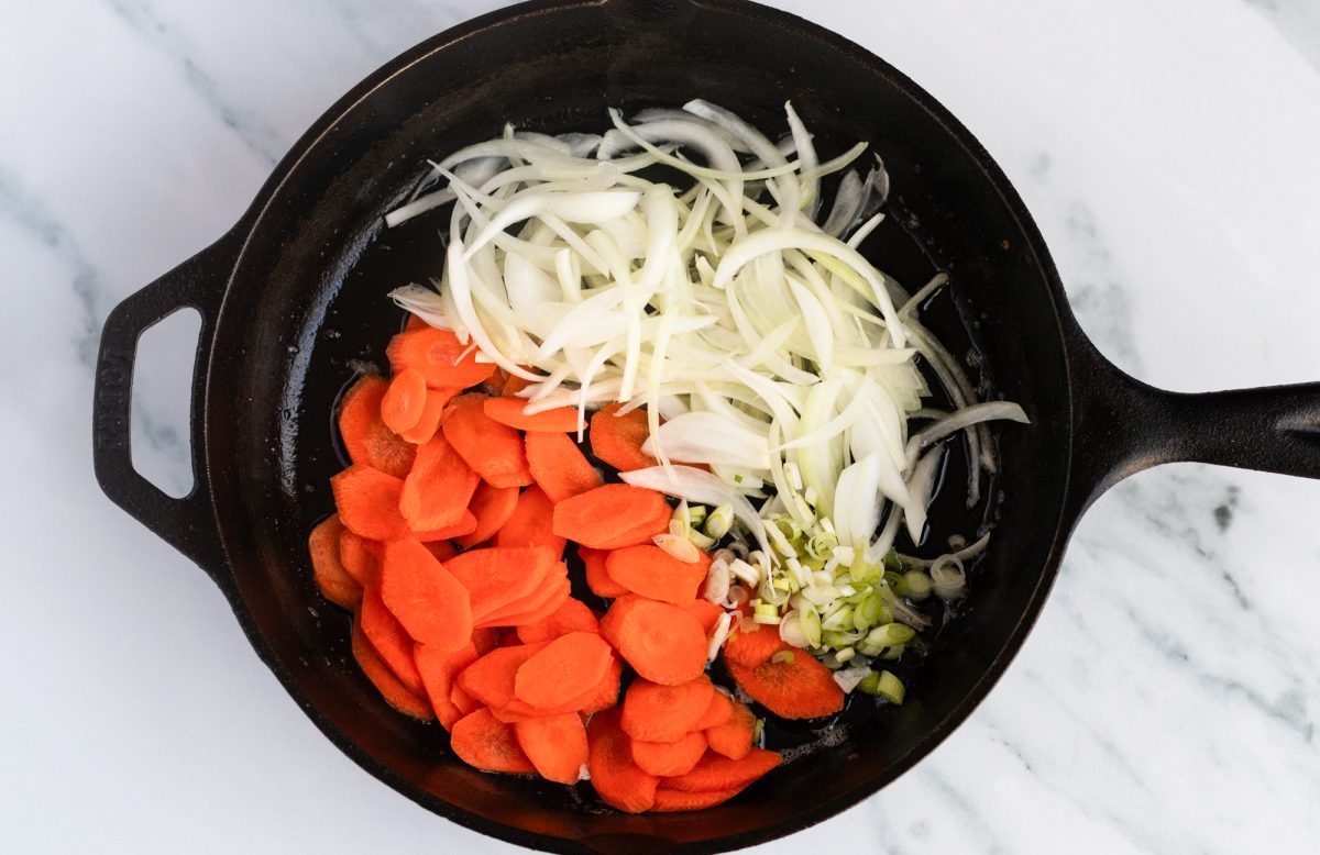 adding carrots, onions, and scallions to cast iron skillet