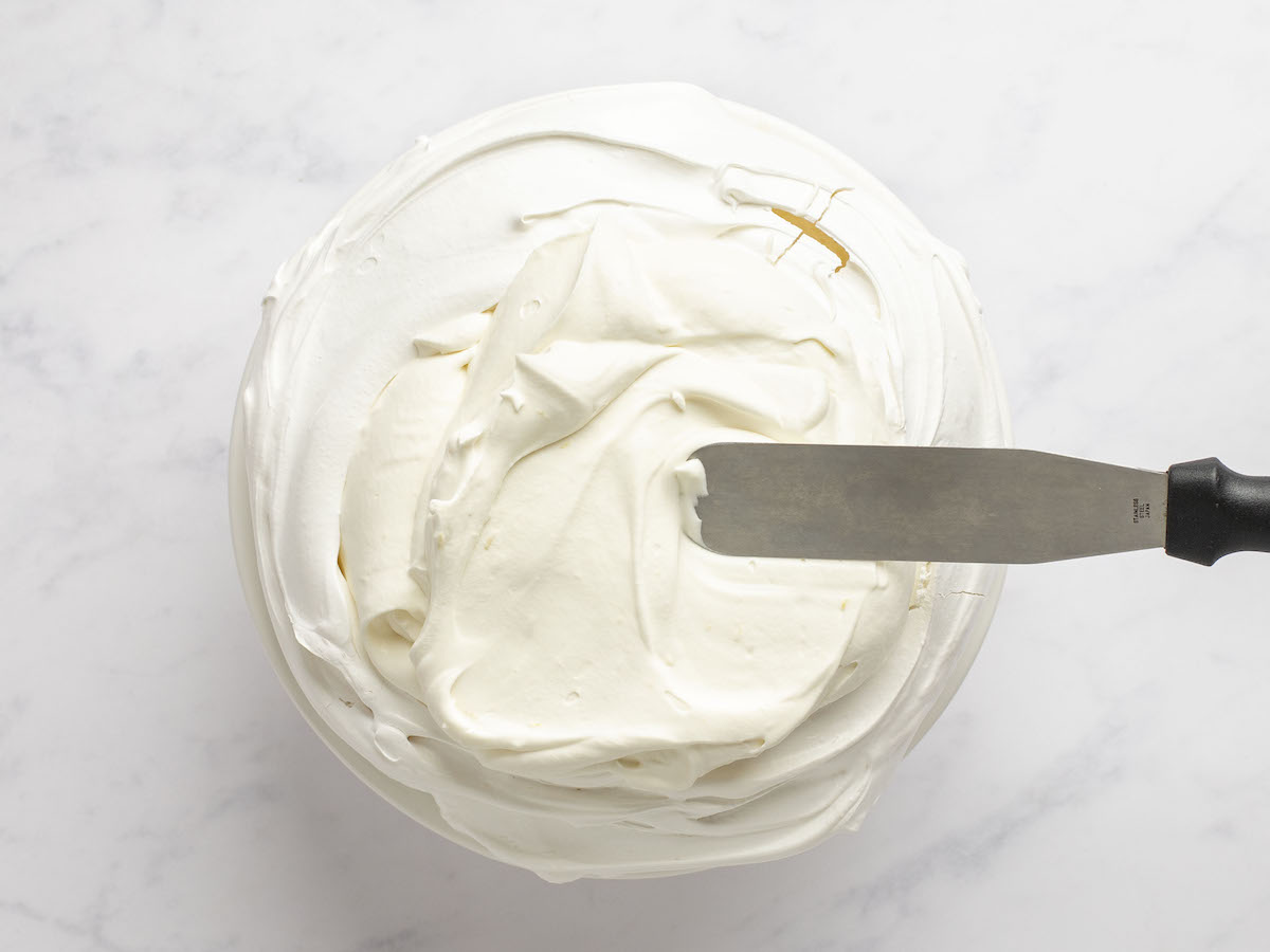 spatula spreading whipped mascarpone cream onto meringue