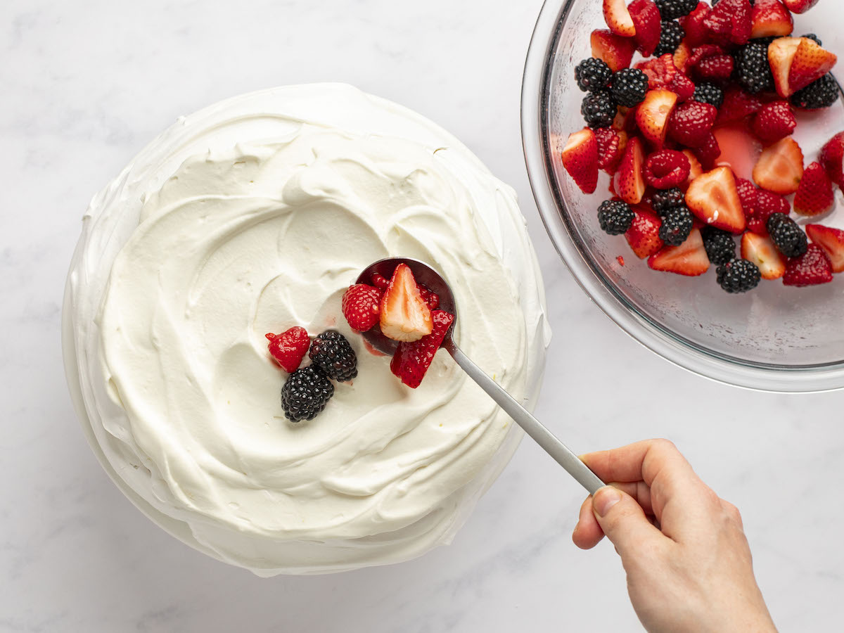 assembling the pavlova by spooning berries over cream.