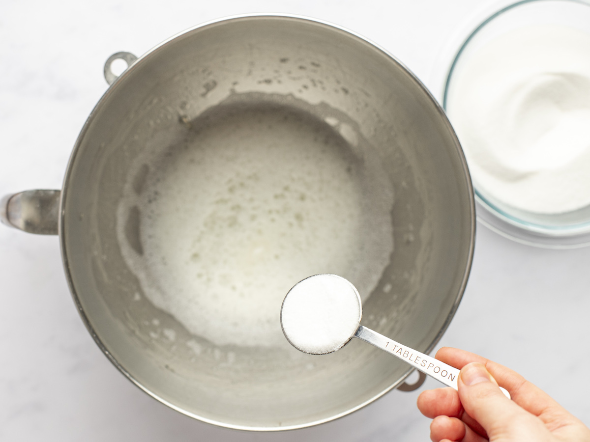 adding sugar to beaten egg whites, salt, and cream of tartar in mixing bowl