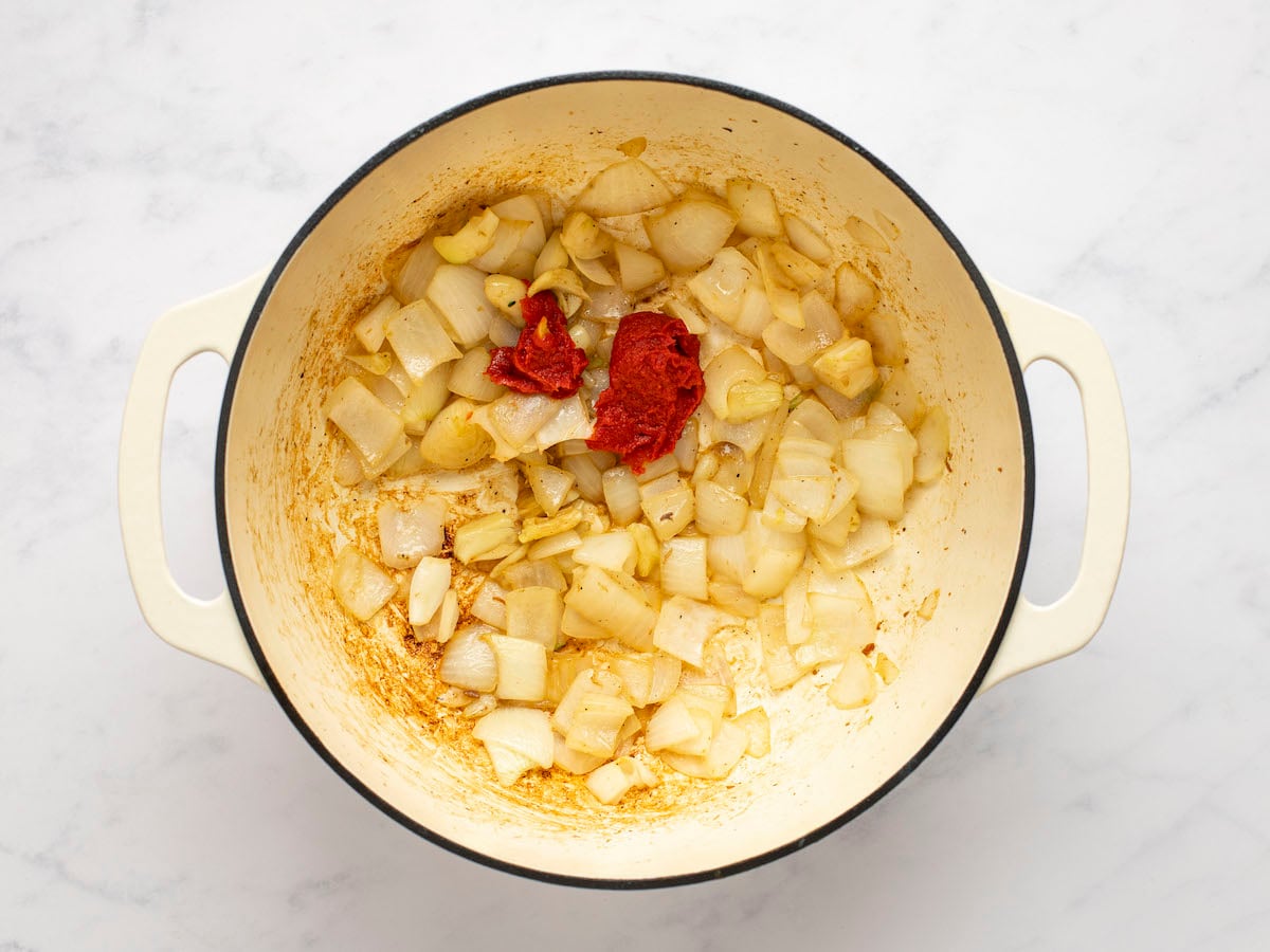 adding tomato paste to onions and garlic in Dutch oven