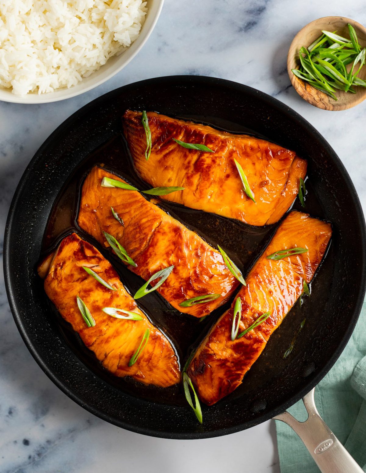 teriyaki salmon in skillet with bowl of white rice and scallions.