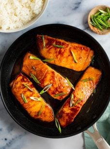 teriyaki salmon in skillet with bowl of white rice and scallions.