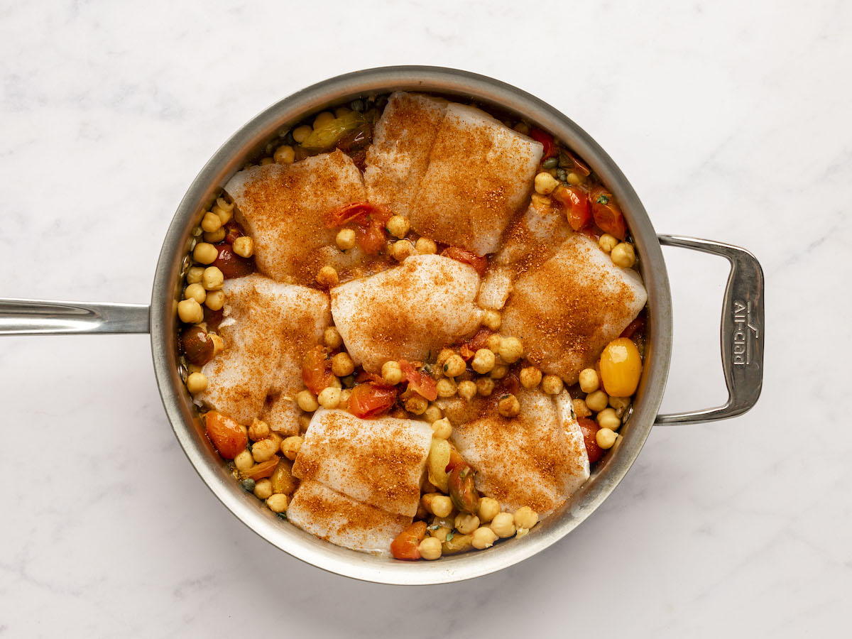 salt and paprika sprinkled overtop the cod in the large pan with tomato chickpea mixture