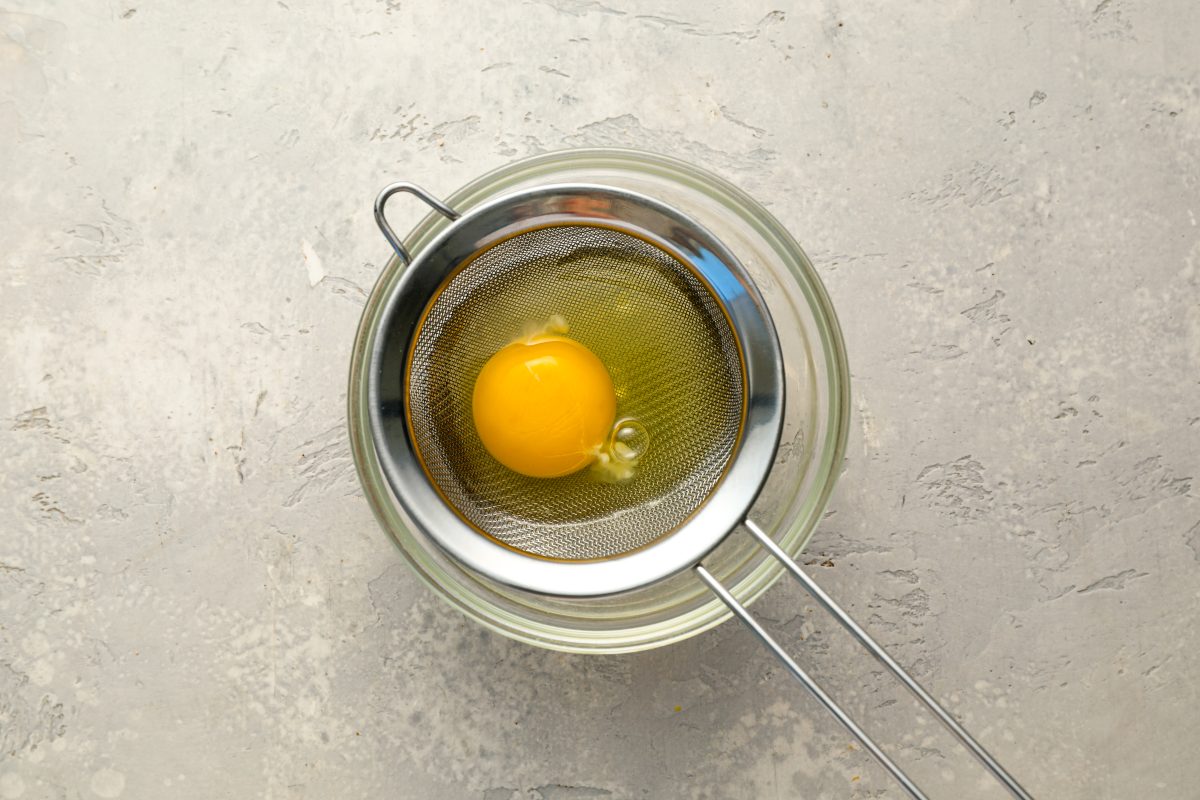 egg in fine mesh sieve over bowl