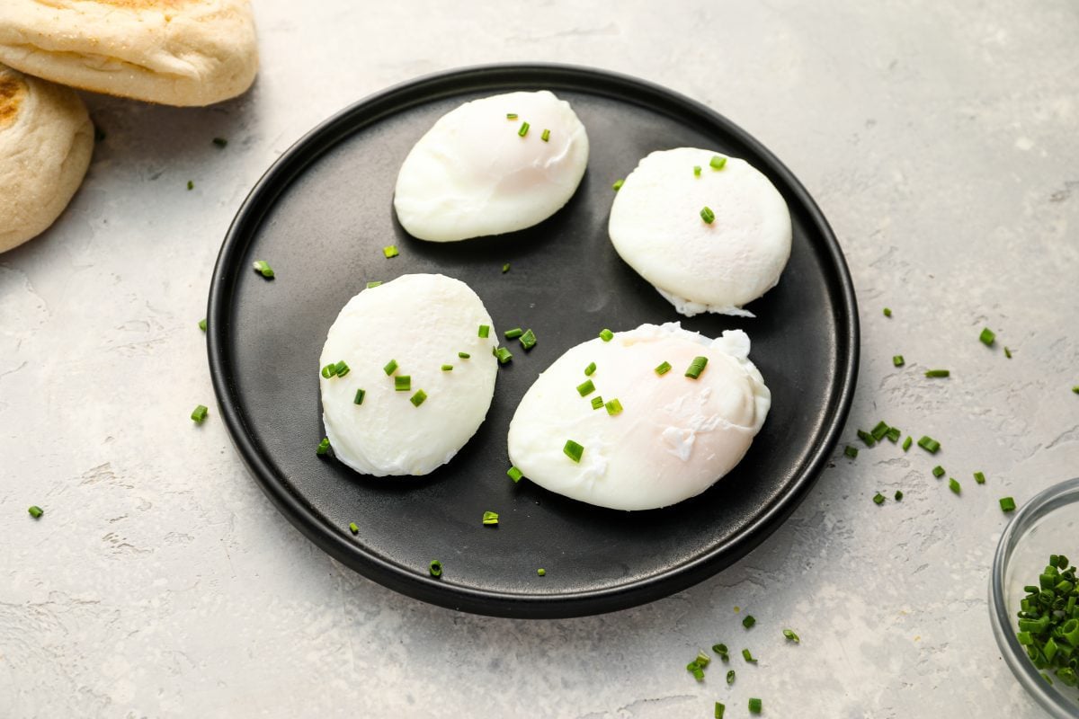 4 poached eggs on a black plate topped with chopped chives