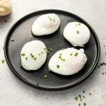 4 poached eggs on a black plate topped with chopped chives