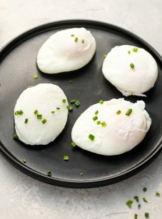 4 poached eggs on a black plate topped with chopped chives