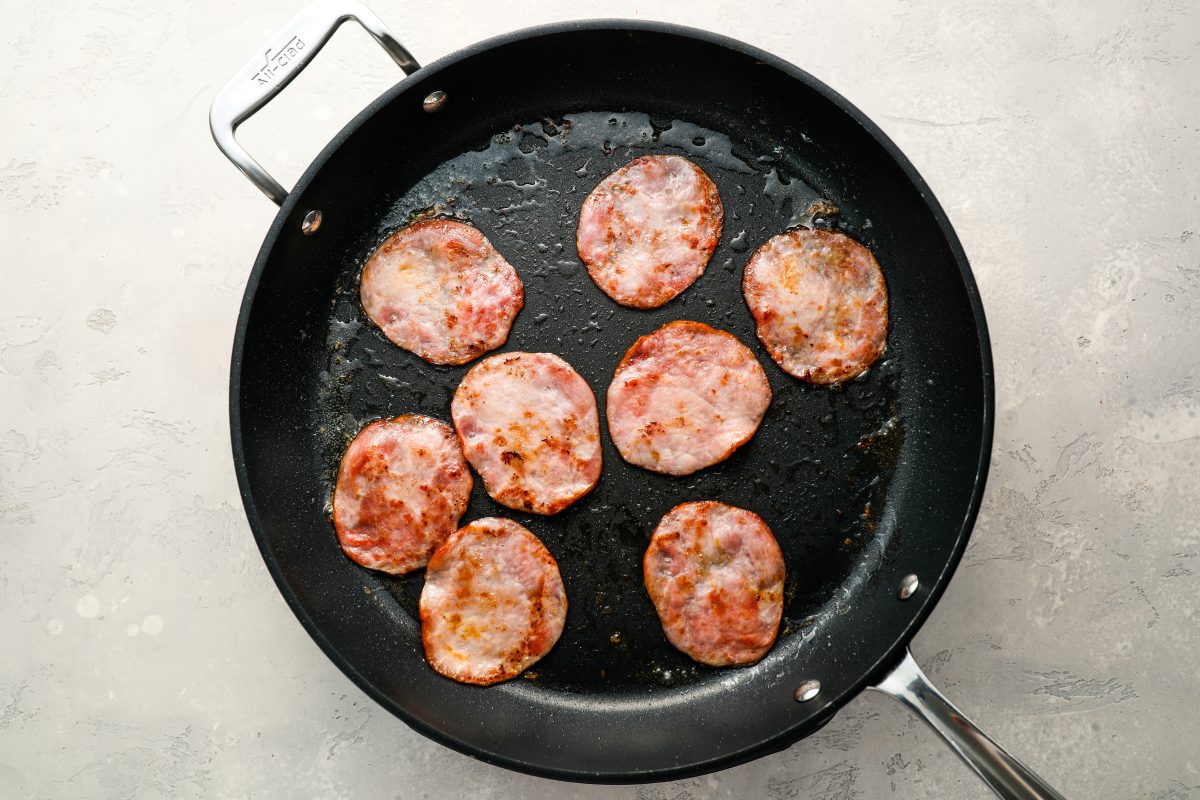 canadian bacon cooking in medium skillet