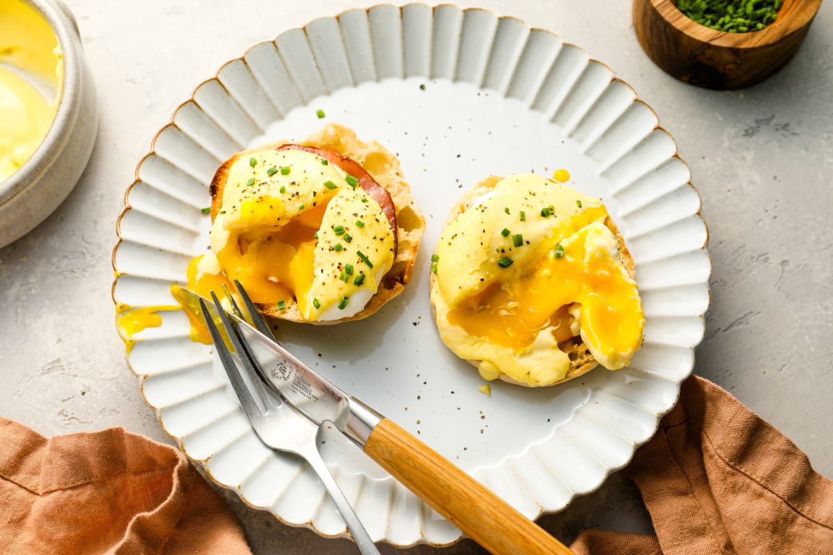 assembled eggs Benedict with runny yolks on white plate with fork and knife