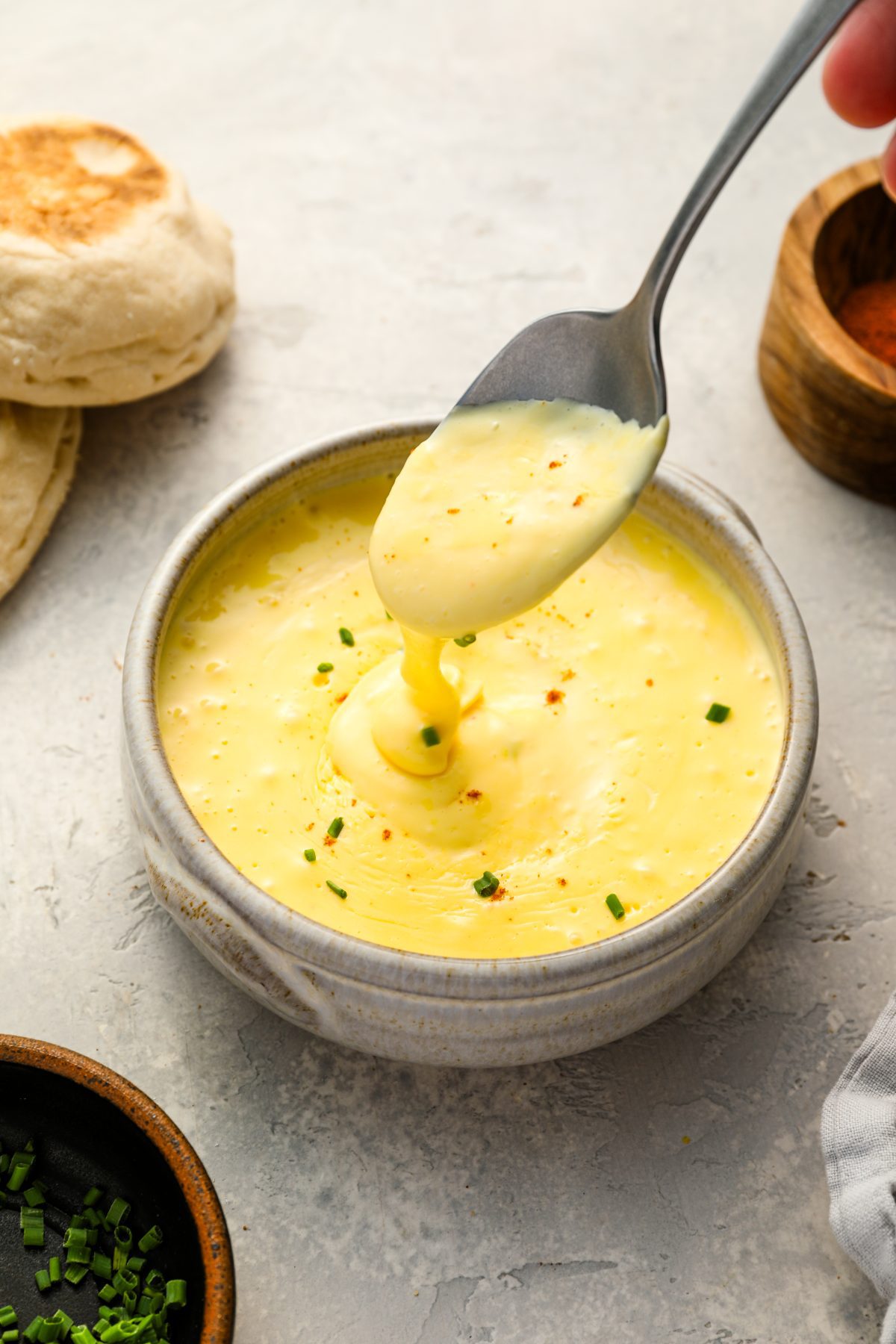 hollandaise sauce topped with chives in bowl with spoon drizzling the sauce into the bowl