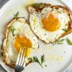 2 crispy fried eggs on white plate with fork poking into runny yolk