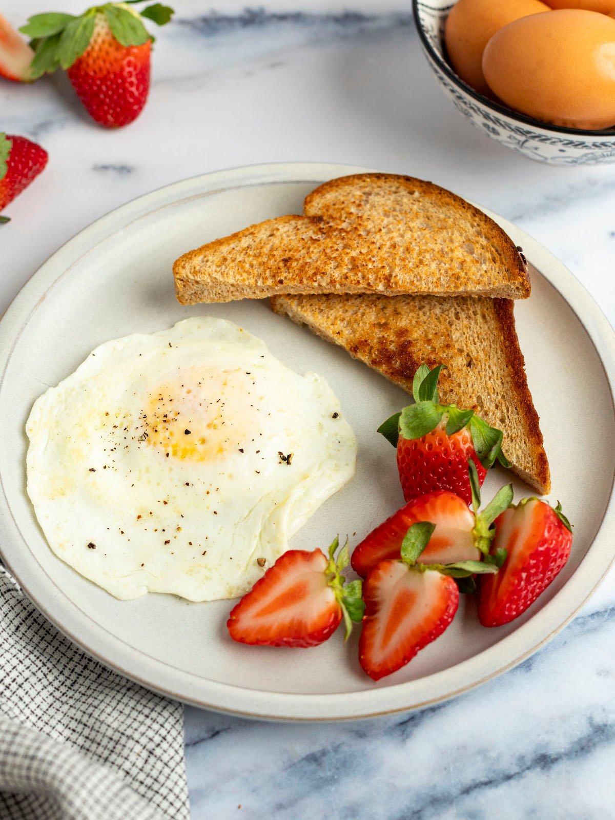 over easy egg on white plate with strawberries and 2 triangles of toast