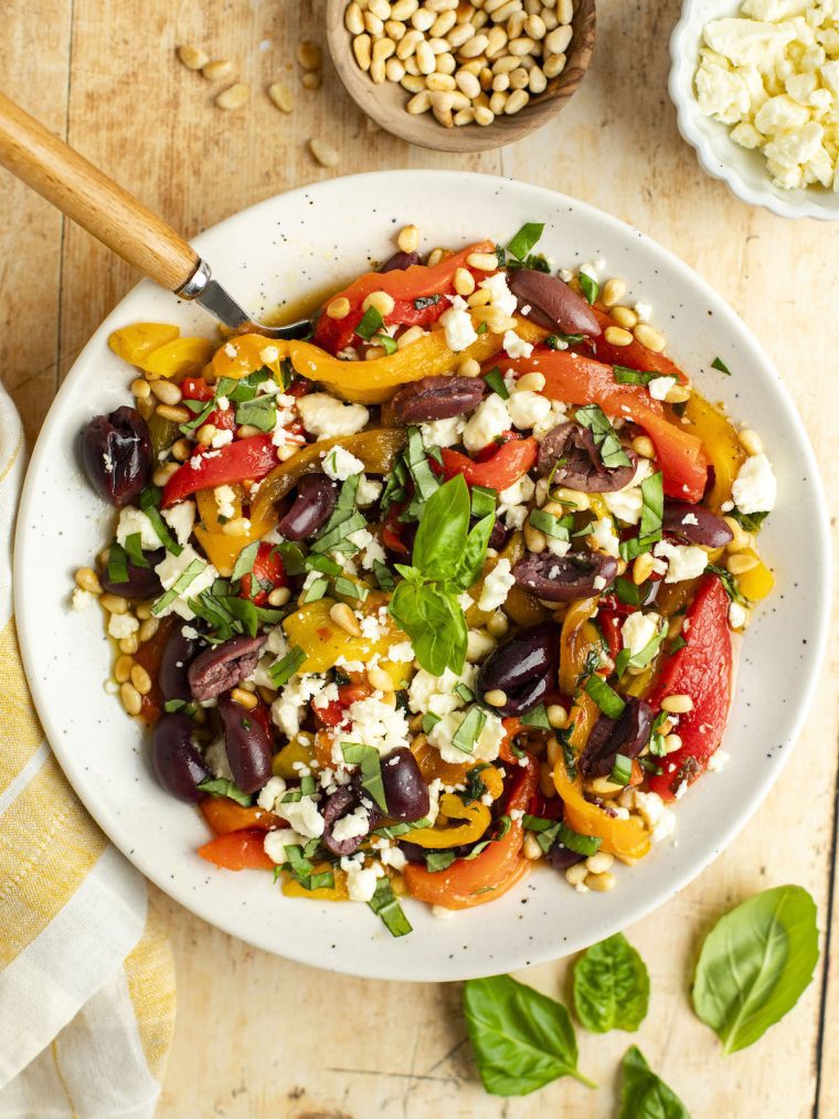 roasted pepper salad in white bowl with basil, pine nuts, olives, and feta cheese.