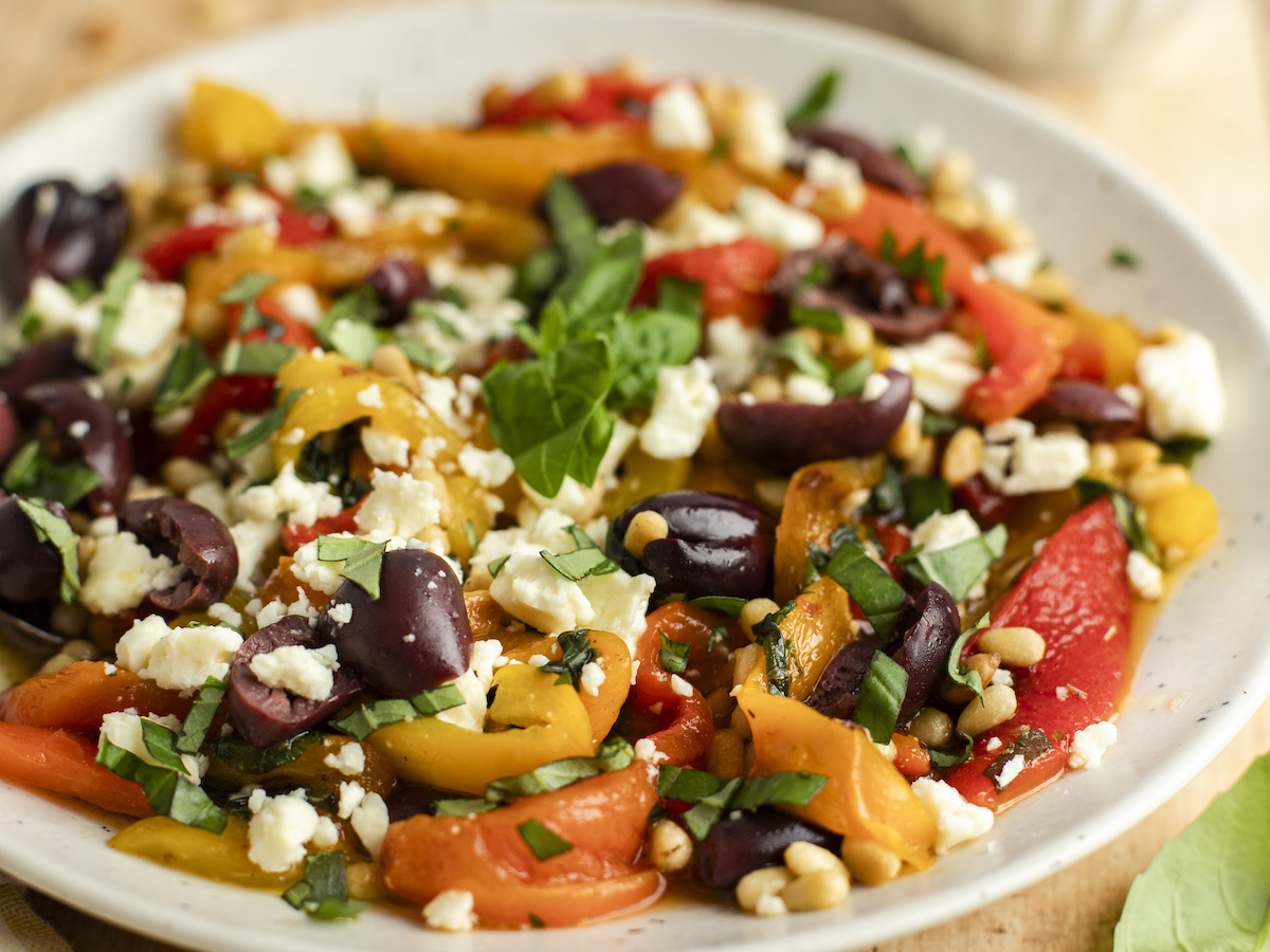 roasted pepper salad in white bowl with basil, pine nuts, olives, and feta cheese.