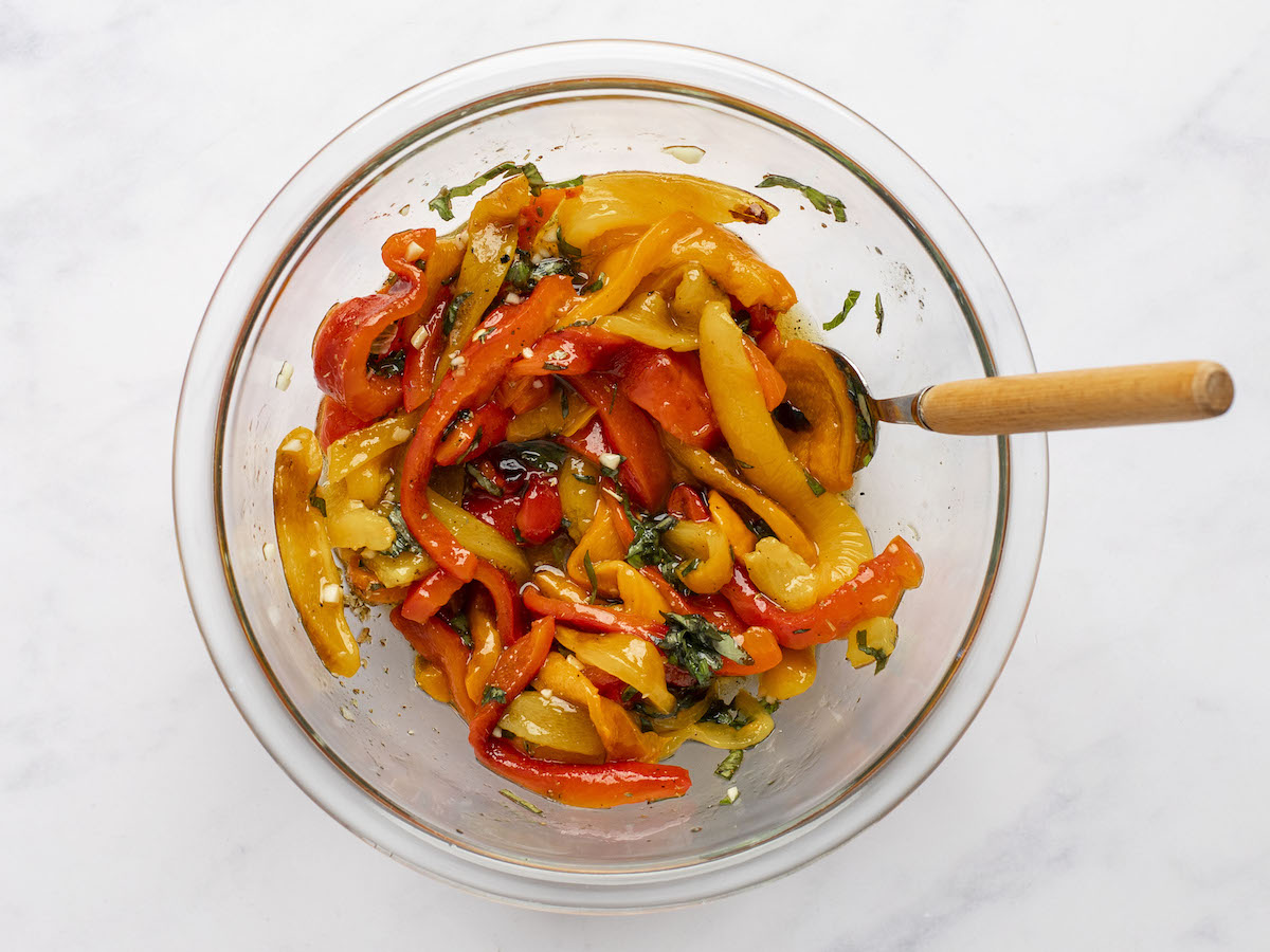 tossing roasted pepper salad in bowl with spoon.