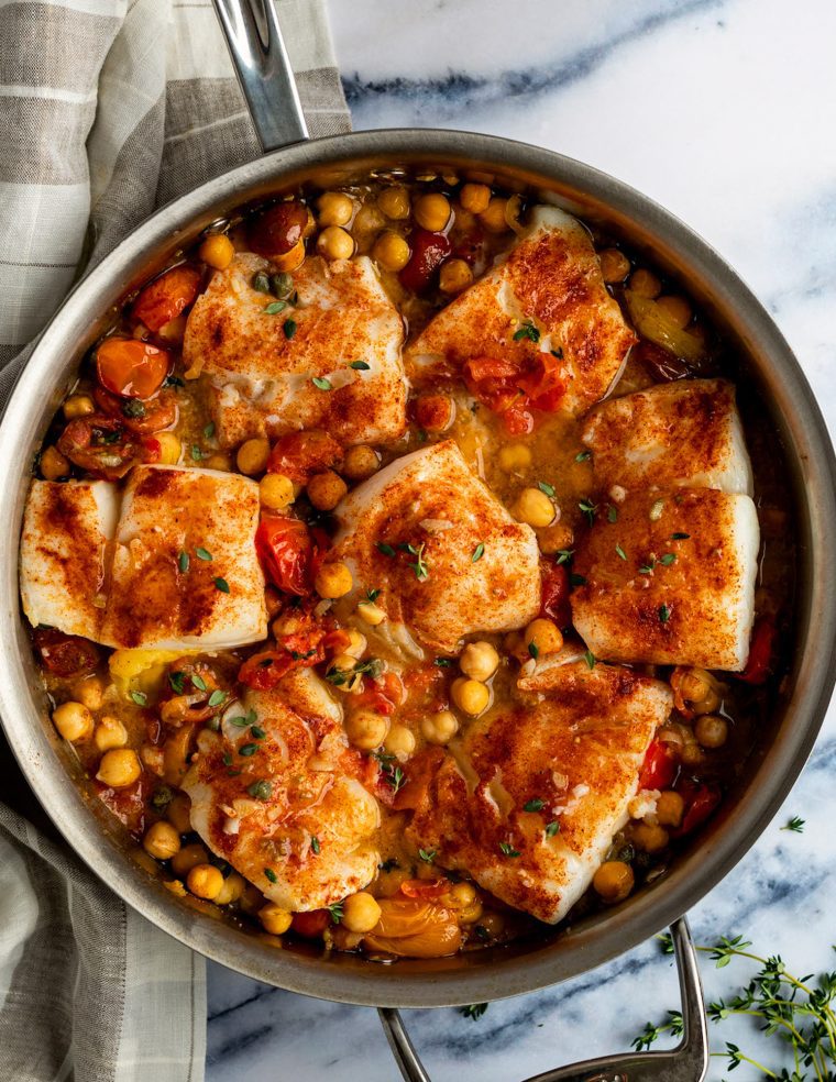 baked cod with tomatoes and chickpeas in skillet with plaid linen napkin