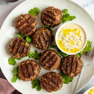 Grilled Moroccan meatballs with yogurt sauce on white platter.