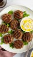 Grilled Moroccan meatballs with yogurt sauce on white platter.