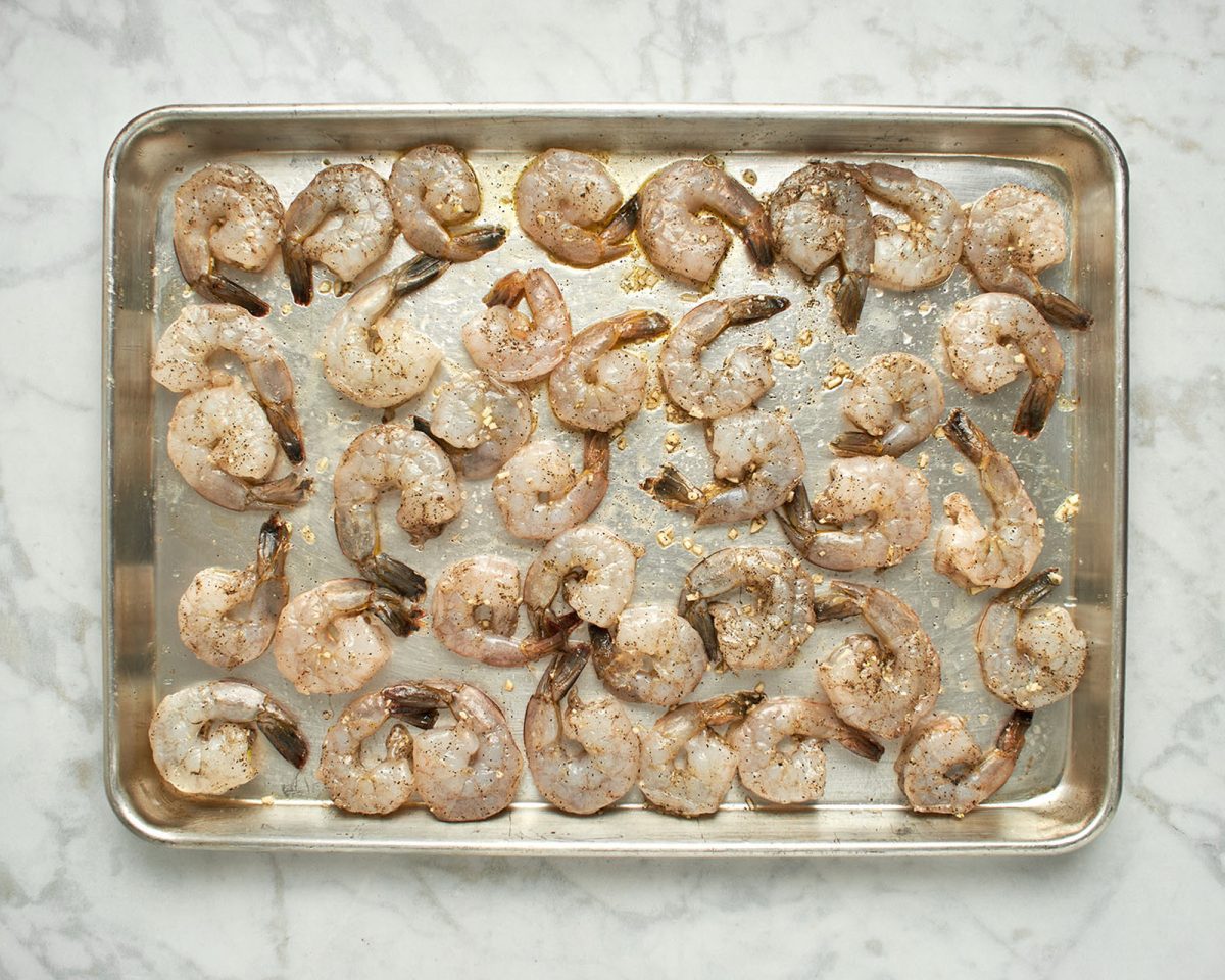 shrimp tossed with olive oil, garlic, and seasoning on baking sheet.