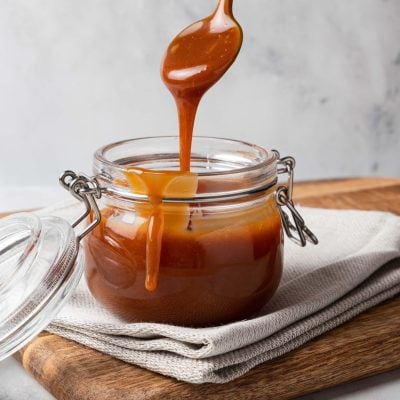 Jar of homemade caramel sauce on wooden board