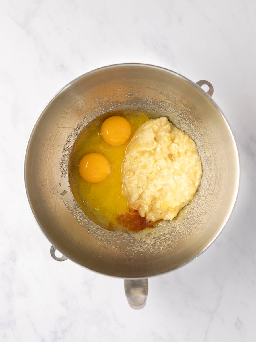 eggs, banana, and vanilla added to melted butter and sugar in metal mixing bowl