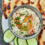 bowl of baba ganoush on platter with cucumber slices and pita bread