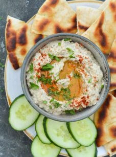 bowl of baba ganoush on platter with cucumber slices and pita bread
