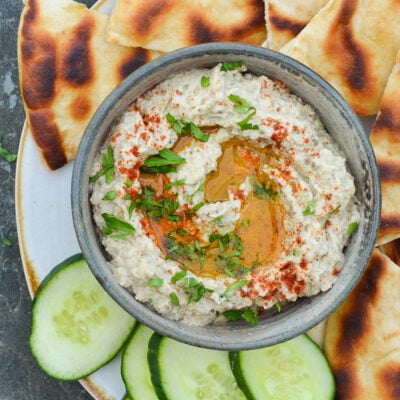 bowl of baba ganoush on platter with cucumber slices and pita bread