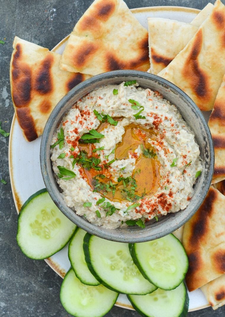 bowl of baba ganoush on platter with cucumber slices and pita bread