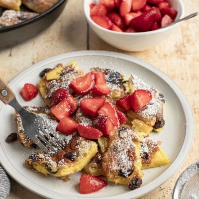 confectioner sugar dusted kaiserschmarrn on white plate with strawerry pieces scattered on top