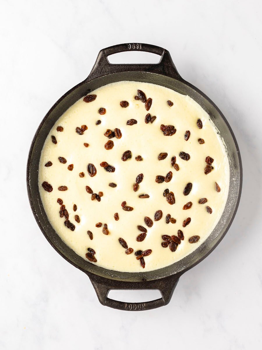 10-inch skillet with rum-steeped raisins evenly distributed in partially cooked batter