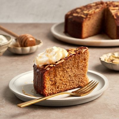 honey cake on platter with bowls of whipped cream, honey and almonds