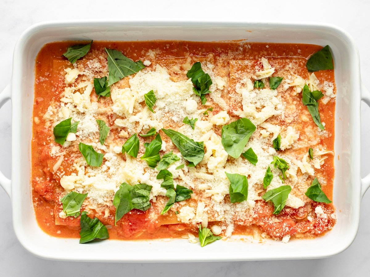 layering cheese lasagna with sauce, noodles, cheese and basil.